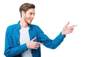 señalando el espacio de la copia. apuesto joven apuntando hacia otro lado y sonriendo mientras está de pie contra el fondo blanco foto