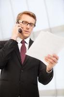 Discussing a report. Confident senior man in formalwear talking on the mobile phone and looking at the documents photo