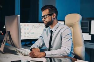 Confident young man working on computer while staying late in the office photo