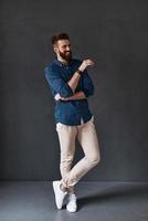 This is interesting Full length of handsome young man looking away and keeping arms crossed while standing against grey background photo
