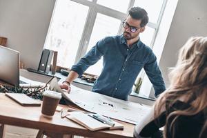 Confident and smart. Two young modern business people in smart casual wear using blueprint while working in the creative working space photo