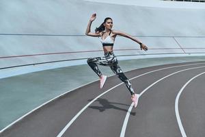 Determined to win. Full length of young woman in sports clothing jumping while exercising outdoors photo