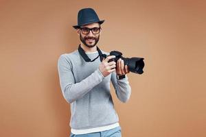 Handsome young man in casual wear looking at camera and smiling while standing against brown background photo