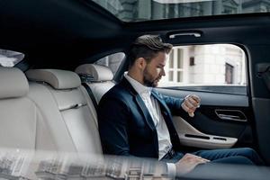 Just in time. Handsome young man in full suit looking at his watch while sitting in the car photo