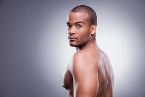 Confident and handsome. Young shirtless African man looking over shoulder while standing against grey background photo