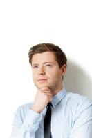 In search of inspiration. Thoughtful young man in shirt and tie holding hand on chin and looking away while standing isolated on white photo