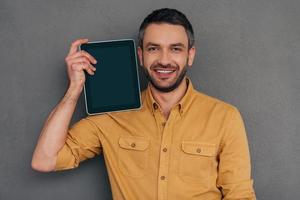 Copy space on his tablet. Handsome mature man carrying digital tablet and smiling while standing against grey background photo