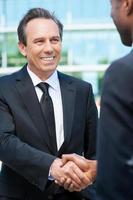 Sealing a deal. Two business men shaking hands and smiling while standing outdoors photo