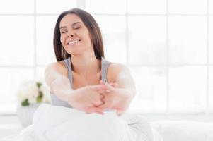 Starting a day from stretching. Beautiful young smiling woman stretching out in bed and keeping eyes closed photo