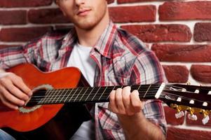 Young virtuoso. Close-up of handsome young man playing acoustic guitar while leaning at the brick wall photo