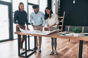 Brainstorming together. Full length of young confident business people discussing something while looking at blueprint in the office photo