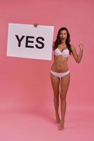 Full length of attractive young woman holding a poster and shouting while standing against pink background photo