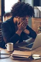 What have I done Young African man looking exhausted and covering his face with hands while sitting at his working place photo