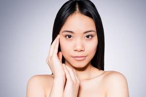 salud y Bienestar. retrato de una hermosa mujer asiática joven y sin camisa tocándose la cara mientras se enfrenta a un fondo gris foto