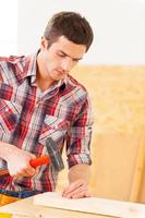 martillando un clavo. apuesto joven manitas martillando un clavo a una cubierta de madera foto