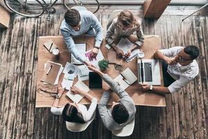 Successful professionals. Top view of young modern men in smart casual wear shaking hands while working with their colleagues in the creative office photo