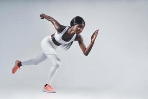 Beautiful young African woman in sports clothing running against gray background photo