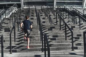 Full length rear view of young man in sports clothing running up the stairs while exercising outside photo