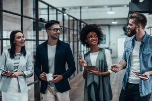 Friendly business chatter. Full length of young colleagues in smart casual wear discussing something while standing in office hallway photo