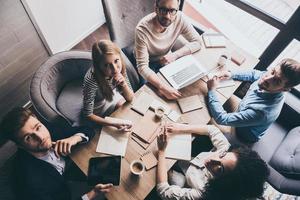 Successful team. Top view of young business people looking at camera while sitting at the office table together photo