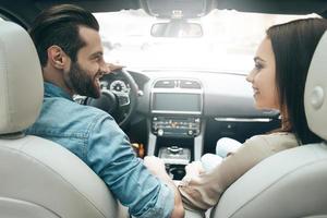 Enjoying the moment. Rear view of young couple sitting on the front passenger seats and looking at each other while handsome man driving a car photo