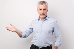 Presenting your product. Confident senior man in formalwear pointing away and looking at camera while standing against white background photo