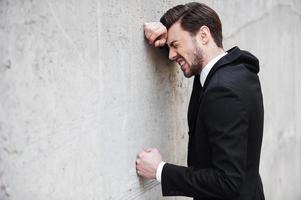 Depressed businessman. Side view of depressed young man in shirt and tie leaning at the wall and keeping eyes closed photo