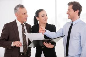 I think it is a good deal. Three confident business people discussing something while woman holding documents photo