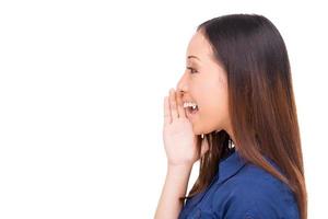 Sharing good news. Side view of beautiful young Asian woman shouting and holding hand near mouth while standing isolated on white photo