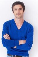 Casually handsome. Handsome young man in blue sweater looking at camera and smiling while standing against grey background photo