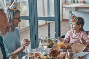 Happy family celebrating birthday of little girl while sitting at the dining table at home photo