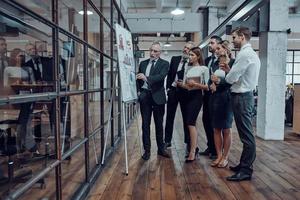 Full length of modern businessman showing graph on the flipchart while having staff meeting in the office corridor photo