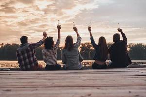 Group of young people in casual wear taking selfie and smiling while enjoying beach party near the campfire photo