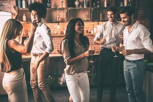 Friends enjoying party . Cheerful young people dancing and drinking while enjoying home party on the kitchen photo