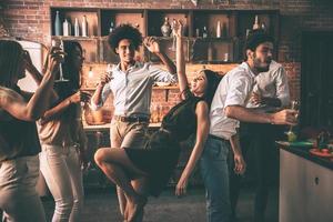 divirtiéndose con amigos. jóvenes alegres bailando y bebiendo mientras disfrutan de una fiesta en casa en la cocina foto