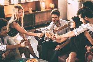 Cheers to best friends ever Top view of cheerful young people enjoying food and drinks while spending nice time in cofortable chairs on the kitchen together photo