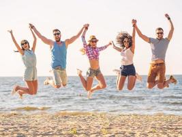 Summer fun. Group of happy young people holding hands and jumping with sea in the background photo