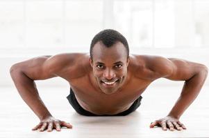 Man doing push-ups. Young muscular African man doing push-ups and looking at camera photo