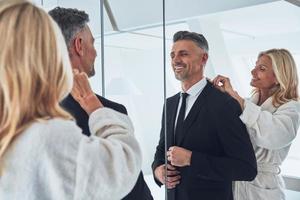 Beautiful mature woman adjusting suit of her husband while both standing in front of the mirror at home photo