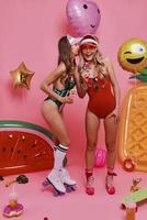 Let the party started Full length of two young women in swimwear covering faces with balloons while standing against pink background photo