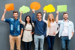 Global communications. Group of happy young people holding empty speech bubbles and looking at camera while standing against grey background photo