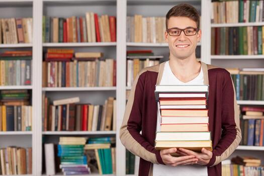 I am ready to my final exam. Cheerful young man holding a book stack and smiling while standing at the library photo