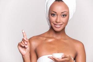 Taking care of her skin. Portrait of beautiful young Afro-American woman wrapped in towel with cream on her finger photo