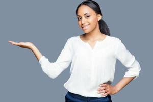 Beautiful woman holding copy space. Attractive young African woman holding copy space on her hand and smiling while standing against grey background photo