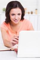 I can learn a lot from the net. Beautiful young woman pointing computer monitor and smiling while sitting at the table photo