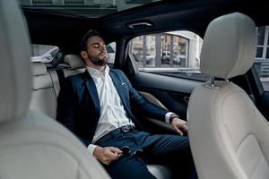 Feeling overworked. Tired young man in full suit keeping eyes closed while sitting in the car photo