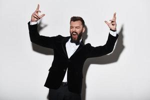 Just going crazy. Handsome young man in full suit making a face and gesturing while standing against grey background photo