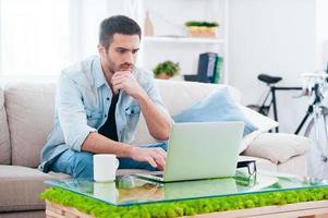 Surfing net at home. Handsome young man working on laptop while sitting on the couch at home photo