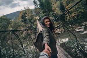 bella joven sonriente tomándose de la mano con su novio mientras caminaba por el puente colgante foto