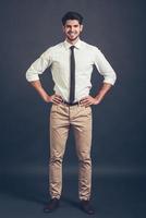 Keep smiling. Full length of confident young handsome man keeping arms akimbo and looking at camera with smile while standing against grey background photo